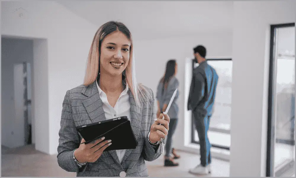 A woman holding an iPad while clients explore a property building in the background