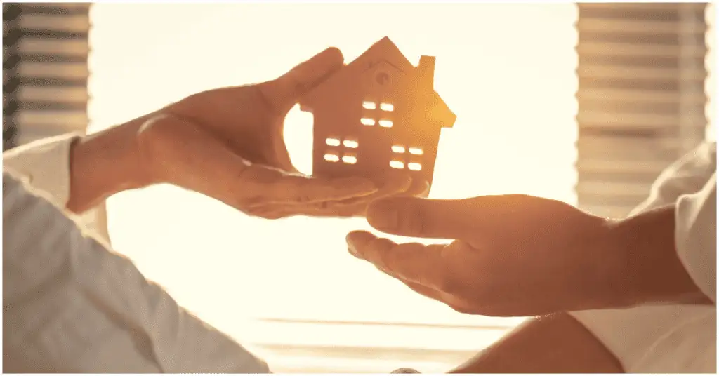 Two people shaking hands while holding a small wooden house, symbolizing collaboration and the importance of your Sphere of Influence in real estate.