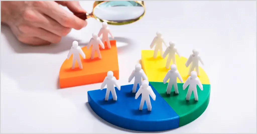 Hand holding a magnifying glass over colorful segments with figurines representing targeted property ads audience segmentation.