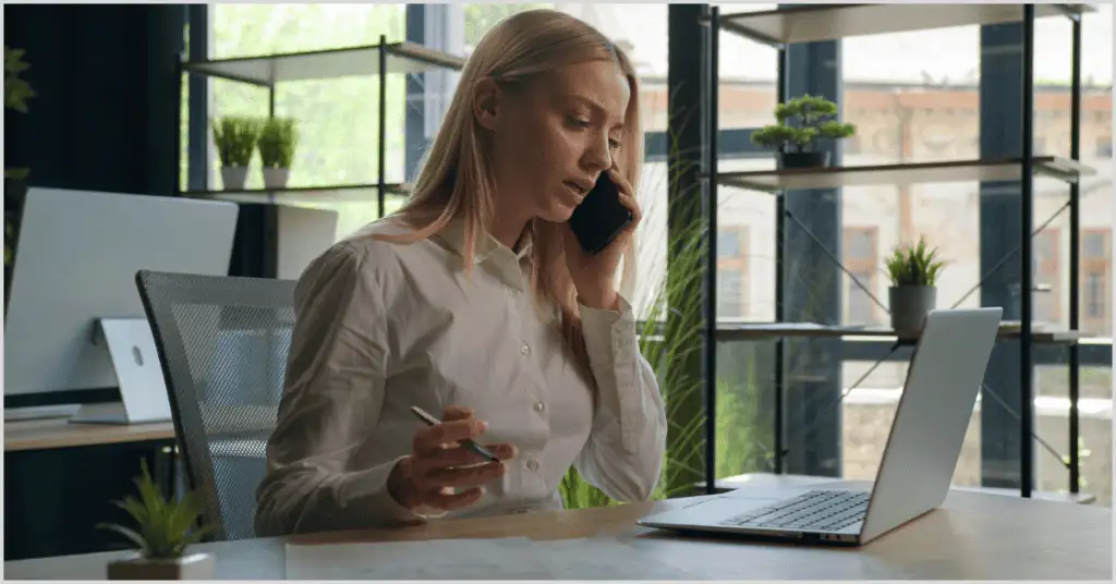 A woman on a phone call with a laptop and papers in a modern office, promoting open house ideas.