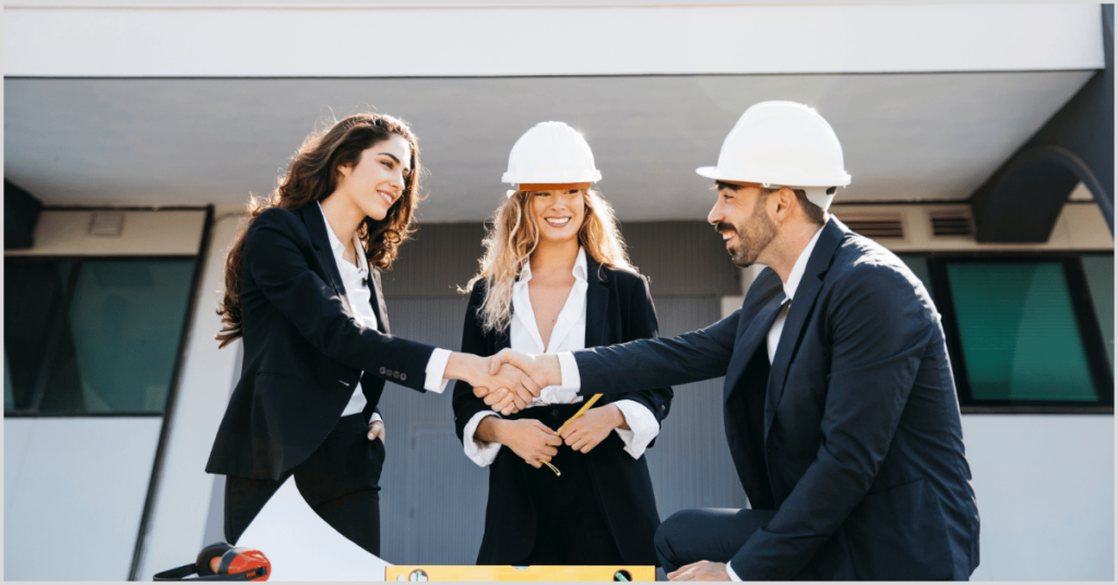 Three professionals in hard hats shaking hands in front of a building, symbolizing partnership with home builders.