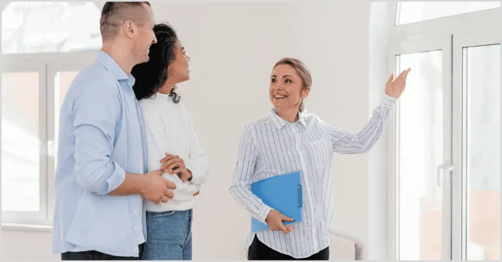 A real estate agent showing a home to a couple, highlighting open house ideas with a clipboard and large windows.