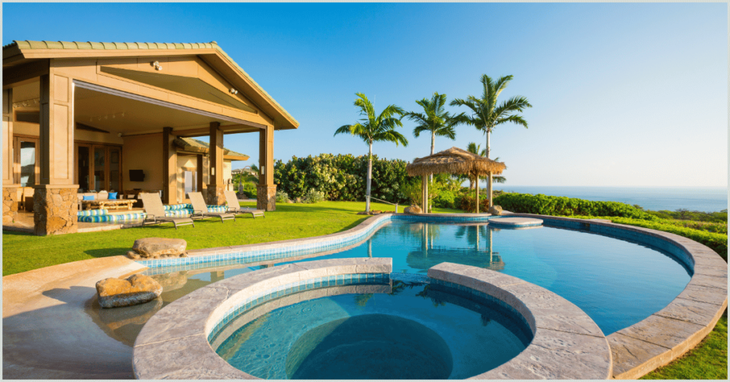 Luxurious house with a curved pool, hot tub, palm trees, and ocean view.