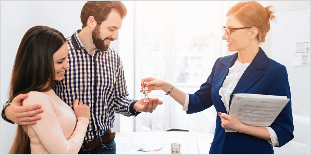 Real estate agent handing keys to a happy couple after closing a deal.