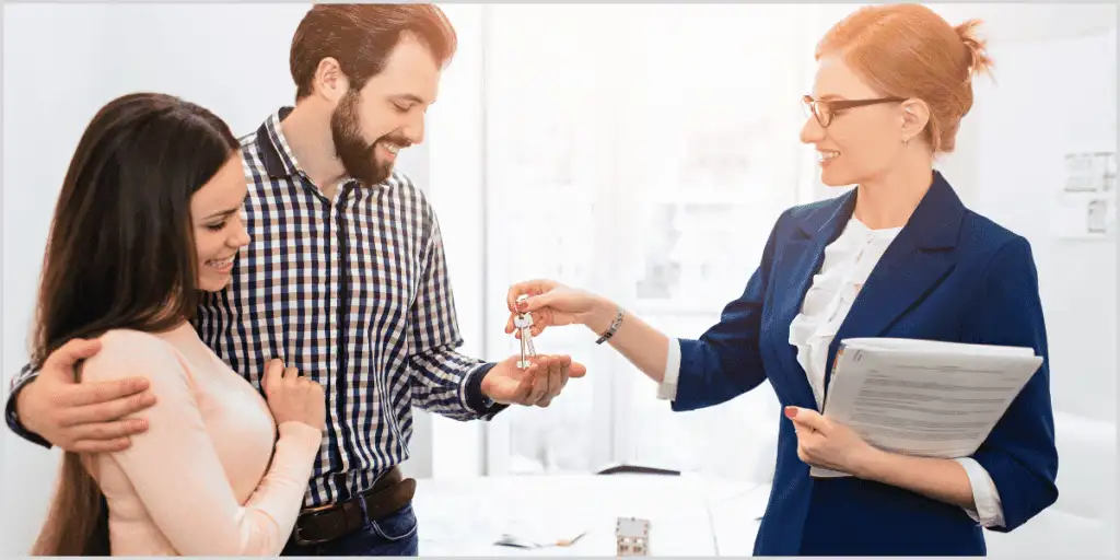 Real estate agent handing keys to a happy couple after closing a deal.