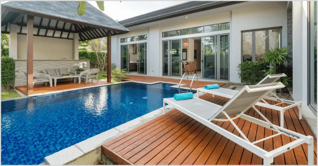 Modern house with a blue pool, wooden deck, lounge chairs, and outdoor seating area.A contemporary house featuring a vibrant pool, wooden deck with lounge chairs, and an outdoor seating area, raising the question of selling difficulty.