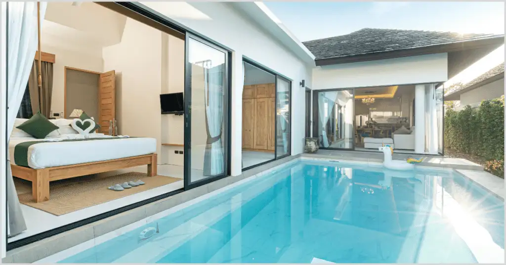 Luxurious bedroom with open glass doors leading to a private pool, featuring a unicorn float.