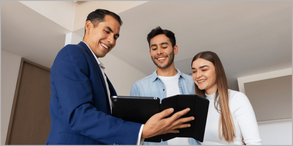 Real estate agent showing property details on a tablet to a smiling couple.