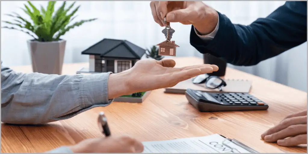 Real estate agent handing keys to client with contract and house model.