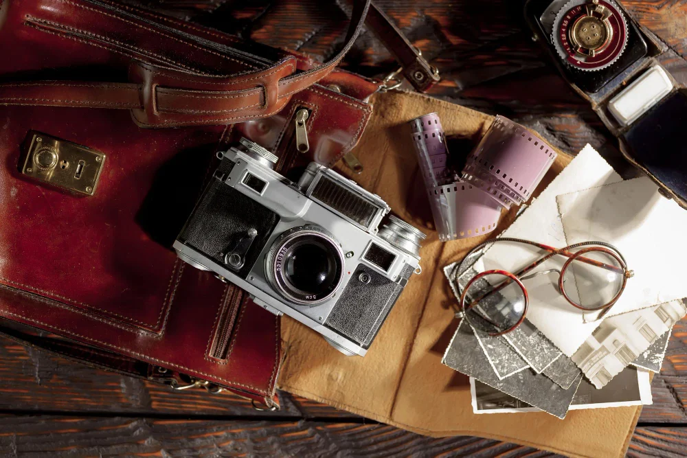 Vintage film camera, rolls of film, old photographs, eyeglasses, and leather bag on a wooden table – perfect illustration of why photography is a good hobby for preserving memories.