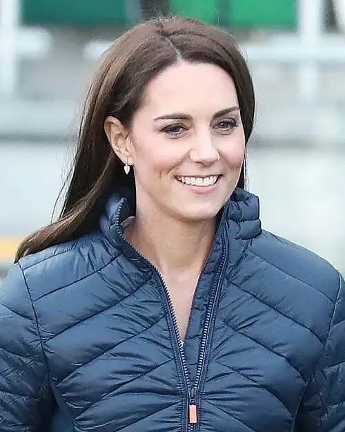 Kate Middleton smiling in navy puffer jacket outdoors, long brown hair and pearl earrings – Who Is The Most Photographed Person In The World