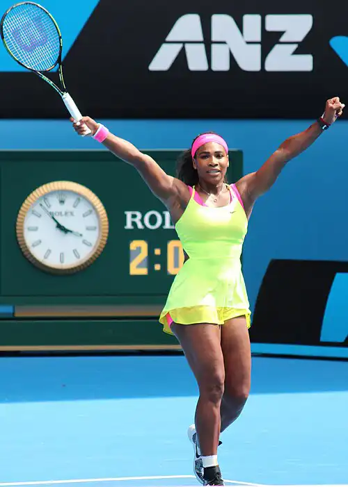 Serena Williams celebrating victory on tennis court, arms raised high in bright neon yellow outfit with racket – Who Is The Most Photographed Person In The World