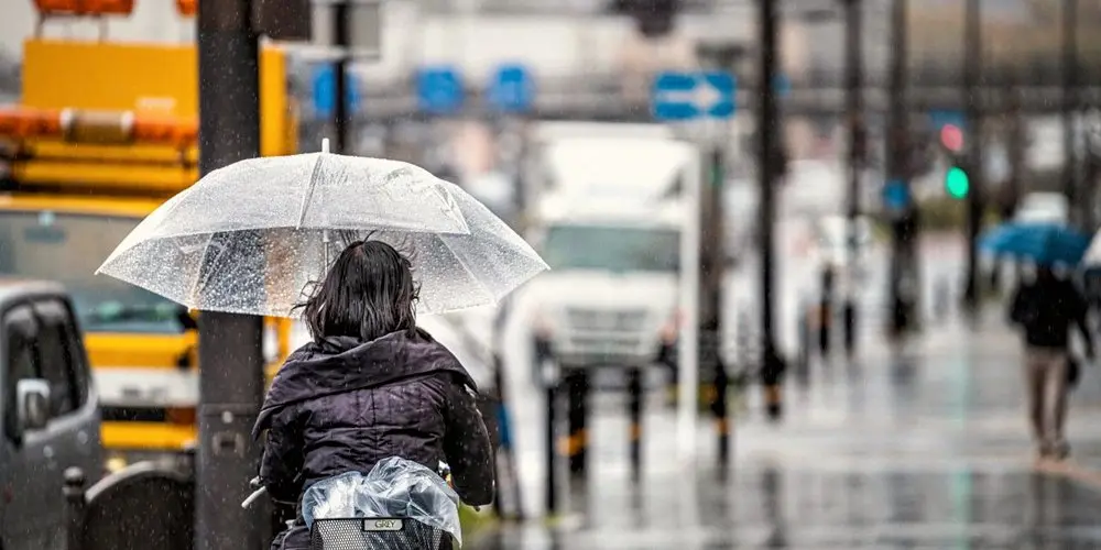 Woman cycling with a transparent umbrella on a rainy city street, a candid example of Realism in Photography