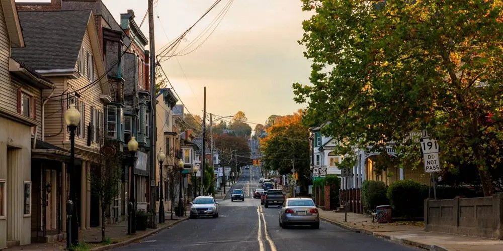 Quiet small-town street with parked cars, houses, and power lines at sunset, example of Street Realism in Photography