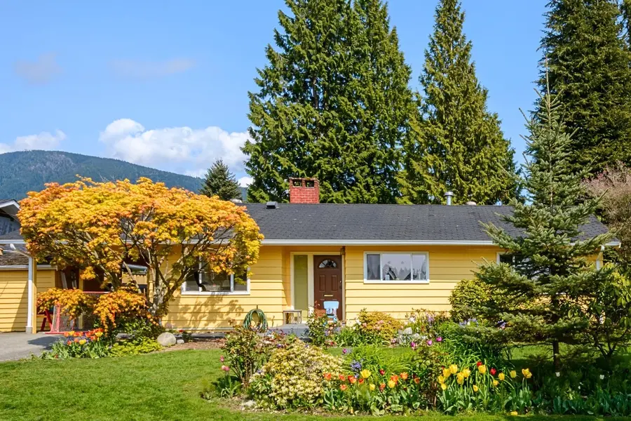 Yellow house with manicured green lawn and colorful flower beds showing treat your lawn like a canvas for landscape curb appeal