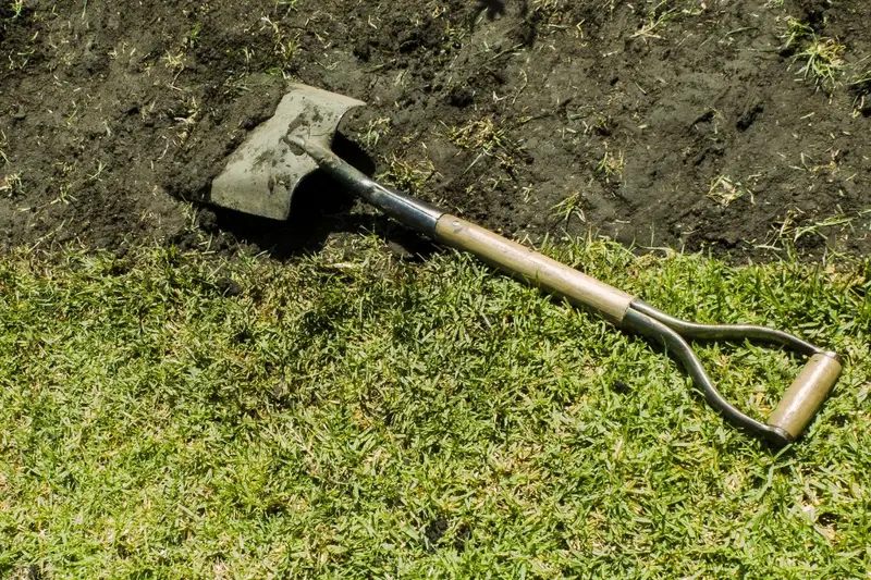 Shovel cutting clean edge between grass and soil to first improve your lawn edging for landscape curb appeal